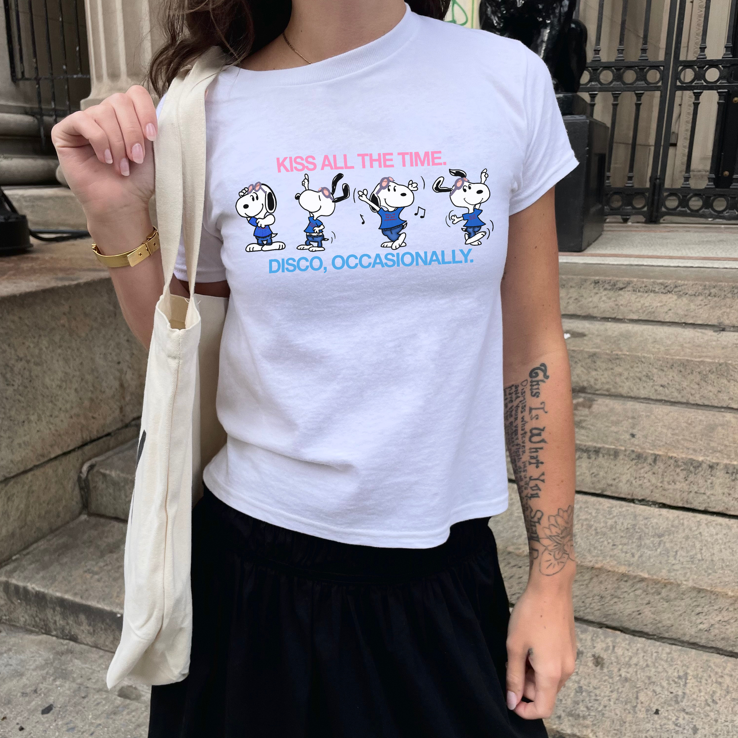 Person wearing a white t-shirt with cartoon characters and text, standing on steps.